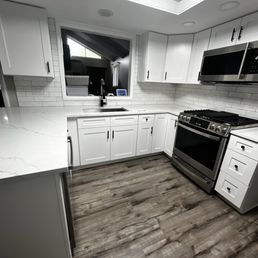 All Done - A kitchen featuring white cabinetry, a marble-patterned countertop, stainless steel microwave and stove, and wood-style flooring.