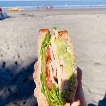 Cheese Shop - a person holding a sandwich on the beach - Sandwiches Near Me - La Jolla, California Cheese Shop - a person holding a sandwich on the beach - Sandwiches Near Me - La Jolla, California