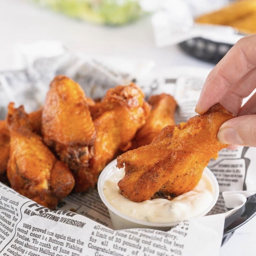 Pomodori - a hand dipping a piece of chicken wings - Pizza Near Me - Ipswich, Massachusetts