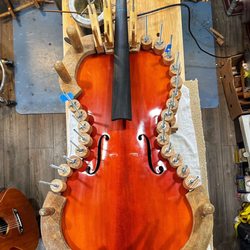 The Unparalleled String Shop - A cello with clamps gluing the top back in place,  a hot glue pot keeps Hide glue liquid state.