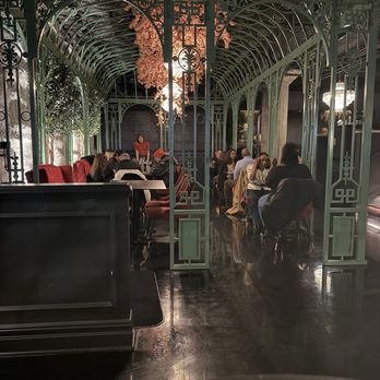 Dearly Beloved - A dining area featuring intricate green metal framework, with patrons seated at tables, some engaged in conversation, and decorative lighting. - Cocktail Bars Near Me - Chicago, Illinois