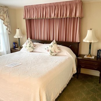 Channel Bass Inn - a bed with a white bedspread and pink drapes - Tea Rooms Near Me - Chincoteague, Virginia