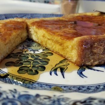 The Bread Boss - Beautiful french toast made with Bread Boss Italian loaf. That crust holds all the eggy, custardy goodness inside while cooking. #sotasty - A slice of French toast with a crispy, golden-brown exterior is placed on a decorative blue and white ceramic plate featuring a grapevine design. The toast appears thick and fluffy inside, with a slightly caramelized surface. Some syrup or butter is visible on the plate, indicating it is ready to be eaten. The background shows a blurred dining setting. - Pizza Near Me - Johnston, Rhode Island