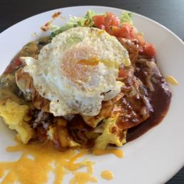 Breakfast Enchiladas - A breakfast dish featuring enchiladas topped with a fried egg, accompanied by diced tomatoes and shredded lettuce on a white plate.