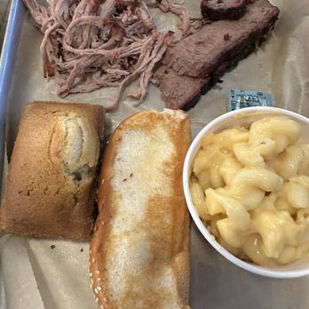 City Barbeque - The image shows a metal tray containing shredded beef, a slice of smoked brisket, a bread roll, a toasted bun, and a cup of macaroni and cheese. The shredded beef and brisket are placed at the top, with the bread roll and toasted bun positioned below, and the macaroni and cheese in a white cup on the right side. The tray appears to be part of a barbecue meal, with the food items arranged for serving. - Barbeque Near Me - Lafayette, Indiana