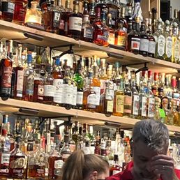 a man and a woman standing in front of a wall of liquor bottles a man and a woman standing in front of a wall of liquor bottles