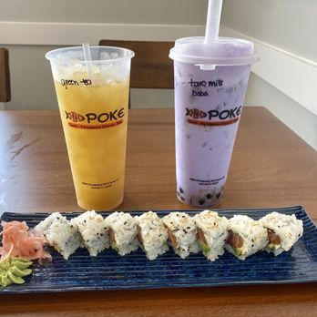 Ono Poke - Parrish roll and drinks - A yellow drink and a purple drink with straws are placed on a wooden table, along with a sushi roll on a black rectangular plate, at Ono Poke in Parrish, FL. - Poke Near Me - Parrish, Florida