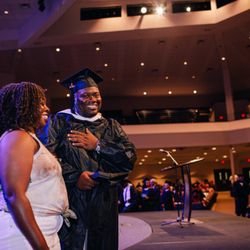 A graduate shares a joyful moment with a guest during Amberton University's commencement ceremony.