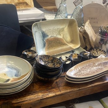 Art Effect - A collection of ceramic bowls, plates, and glass bottles arranged on a wooden table in a retail setting. - Women's Clothing Near Me - Chicago, Illinois