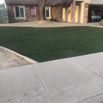 The Yard Guys - A single-story house with a brick facade, a large tree in the front yard, and an American flag hanging near the window. - Tree Services Near Me