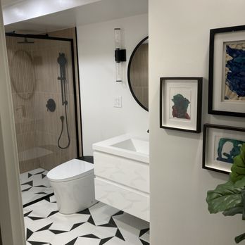 Dream House Services - His most recent work is a basement bathroom. He helped settle the design and scale of everything. Came out perfect. - This bathroom includes a walk-in shower with a black frame and beige tiles, a white vanity with a geometric pattern, and a round mirror. The floor has black and white geometric tiles, and there are framed artworks on the wall near the vanity. The space appears modern and well-designed. - General Contractors Near Me - Randolph, Massachusetts
