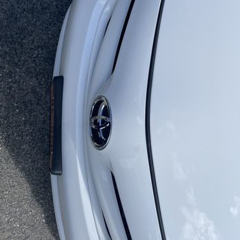 NTC Auto Body - After front bumper - The image shows the front section of a white Toyota vehicle, including the grille with the Toyota emblem prominently displayed in the center. The hood and part of the bumper are visible, with the vehicle parked on a paved surface. The photo captures the vehicle's clean exterior and design details. - Body Shops Near Me - Fishkill, New York