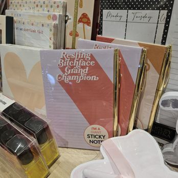 Uncharted - A set of notebooks, including one with humorous text, and gold pens are displayed on a store shelf, with other stationery items visible. - Accessories Near Me - Oak Brook, Illinois