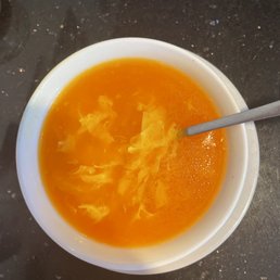 Egg Drop Soup - A bowl of egg drop soup with a spoon, placed on a dark, speckled countertop, showcasing the bright orange broth and swirling egg ribbons.