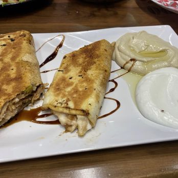 Aleppo Kebab - Chicken shawarma wrap - A plate with two chicken shawarma wraps, one cut open to show the filling, accompanied by two different sauces, likely yogurt and garlic sauce. - Salad Near Me - Ajax, Ontario