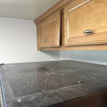 Super Maids - This is how the top of the fridge was left, again supposed to be DEEP cleaning - Crumbs and dust are scattered on a black kitchen appliance surface, with wooden cabinets above in a home kitchen setting. - Home Cleaning Near Me