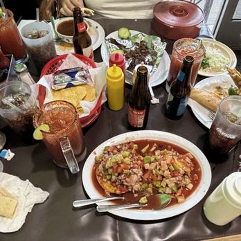 Sin Son Nay - A dining table with various Mexican dishes, including a large plate of ceviche, tacos, and drinks like beer and soda, surrounded by condiments and utensils. - Mexican Near Me - Phoenix, Arizona