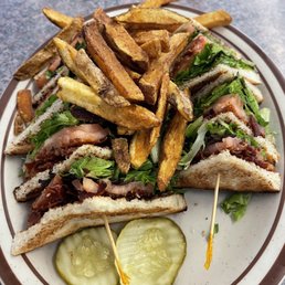 Turkey club with homemade fries - soup is also included. - A plate featuring club sandwiches with lettuce, tomato, and bacon, topped with French fries and two pickle slices.