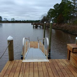 A wooden dock with metal handrails leads down to a floating platform over calm river water...