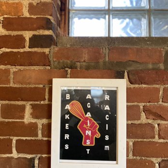Lil's Café - Photo shows framed artwork on a brick wall. The art is of the Black power fist holding a whisk. Lettering says "BAKERS AGAINST RACISM." - Coffee & Tea Near Me - Kittery, Maine Lil's Café - Photo shows framed artwork on a brick wall. The art is of the Black power fist holding a whisk. Lettering says "BAKERS AGAINST RACISM." - Coffee & Tea Near Me - Kittery, Maine
