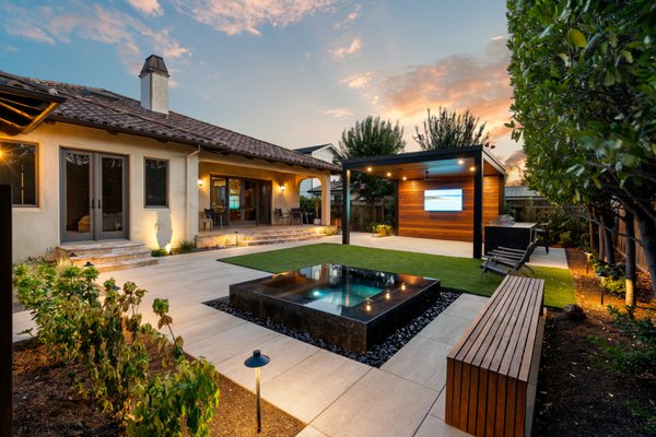 The McBain Project | Backyard Remodel - The McBain project in Willow Glen, CA - Designed and built by R&R Backyard Remodeling, this complete backyard transformation creates multiple spaces for relaxing, entertaining, wellness, and everyday outdoor living. The project features Techo Bloc pavers, artificial turf, custom IPE wood details, lush landscaping, and integrated low voltage lighting throughout.
A custom raised spa creates a striking focal point, while the main aluminum pergola defines an entertainment area featuring IPE wood cladding, an outdoor TV, integrated lighting, and an outdoor kitchen. A second aluminum pergola creates a dedicated outdoor gym, complete with IPE privacy screening and retractable shades on all four sides for added privacy, shade, and flexibility.
The result is a warm, modern backyard with distinct functional zones connected through consistent materials, architectural details, and thoughtful lighting. Designed and built from start to finish by R&R Backyard Remodeling.