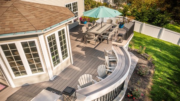 Deck with Curved Bar & Outdoor Kitchen in Harrisburg, PA - This outdoor living space is perfect for summer barbequing or just lounging in the sun! The deck features Azek composite decking and black aluminum railing for a long-lasting and low-maintenance project. The highlight of this project is the curved bar with Provia stone pillars, perfect for morning coffee with friends and family. We installed a Dek Drain dry deck system which will keep the existing patio area dry. The outdoor kitchen is top-of-the-line with stainless steel appliances and a granite countertop. For the finishing touches, we installed post cap lights and step riser lights that add a touch of ambiance to the space. Deck with Curved Bar & Outdoor Kitchen in Harrisburg, PA - This outdoor living space is perfect for summer barbequing or just lounging in the sun! The deck features Azek composite decking and black aluminum railing for a long-lasting and low-maintenance project. The highlight of this project is the curved bar with Provia stone pillars, perfect for morning coffee with friends and family. We installed a Dek Drain dry deck system which will keep the existing patio area dry. The outdoor kitchen is top-of-the-line with stainless steel appliances and a granite countertop. For the finishing touches, we installed post cap lights and step riser lights that add a touch of ambiance to the space.