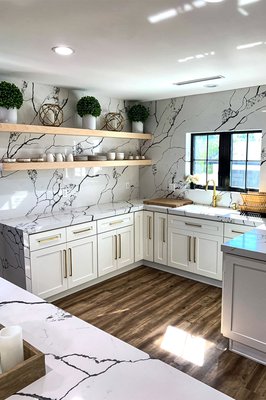 Pasadena Kitchen Remodel - This project started with a small kitchen that had dated wood cabinetry and old-fashioned fixtures and lighting. We worked with our clients to create a bright, spacious, and family-friendly kitchen that flowed directly to a large dining area and huge family room with a fireplace.  This client had excellent taste and a clear vision of what he wanted the space to look like and how it would bring the family together. We began by relocating a shear wall, to add symmetry to the kitchen and create a more modern, spacious area. We installed the oak floors, which contrasted beautifully with the white shaker cabinets, and gorgeous backsplash, which is a whimsical white and black veinous pattern. The large island features a Calacatta white quartz countertop.

The kitchen is easy to cook in, the kids sit at the island, and the family has a choice of dining at the big kitchen table or more casually at the island. The room is full of light and spacious enough for cooking for and entertaining large groups, and the black, gold, and white palette works beautifully with the warmth of the oak hardwood floors.