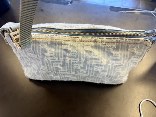 Fendi Zucca Denim Bag: Yellow Staining Removed - This vintage Fendi Zucca shoulder bag in pale blue distressed denim came to us with a yellow stain running along the top and a dingy cast across the front panel. The FF logo on this bag is not printed, it is raised in a frayed cream pile that traps soil between its fibers, so the yellowing had settled into the texture as well as the denim. The striped FF lining inside had gone dull and grubby from years of use. A bag like this never goes into a machine. We spot tested the denim in a hidden area first, then worked the yellow band along the zipper edge in small passes with drying time between them, lifting soil out of the pile with controlled agitation rather than pressure so the logo kept its loft. The striped canvas strap was cleaned separately, since it carries the most hand oil on the bag, and the lining was turned out and cleaned as its own job after testing each dye in the stripe. The FF buckle, zipper, and zipper pull were polished last to bring the shine back. The bag was reshaped and dried slowly away from heat. Handbag cleaning starts at $49.99 for a small bag, and a two-part job like this one started the thumbnail.