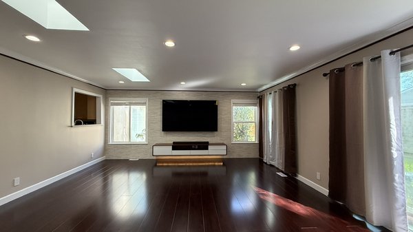 Living room remodel - The remodeled living room combines modern elegance with cozy comfort, creating a welcoming and stylish space perfect for relaxing or entertaining. Neutral tones on the walls provide a calming backdrop, while updated lighting—featuring recessed fixtures—adds warmth and ambiance. A new hardwood floor runs throughout. The focal point of the room is a custom-built media wall with Purestone Murreto Text Beige tiles and a vintage TV console with LED light underneath. Large windows framed by updated drapery bring in natural light, enhancing the room’s airy, open feel. Living room remodel - The remodeled living room combines modern elegance with cozy comfort, creating a welcoming and stylish space perfect for relaxing or entertaining. Neutral tones on the walls provide a calming backdrop, while updated lighting—featuring recessed fixtures—adds warmth and ambiance. A new hardwood floor runs throughout. The focal point of the room is a custom-built media wall with Purestone Murreto Text Beige tiles and a vintage TV console with LED light underneath. Large windows framed by updated drapery bring in natural light, enhancing the room’s airy, open feel.