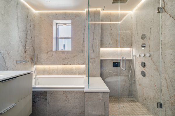 Bathroom Remodeling - Upper East Side - This sophisticated bathroom transformation embodies modern luxury and spa-like serenity. Wrapped in full-height, bookmatched marble-look porcelain panels, the space achieves a seamless and immersive aesthetic. Subtle veining and natural texture in the tile create warmth and depth, while integrated LED cove lighting and vertical vanity illumination add a touch of understated drama.
A floating double vanity in a soft matte finish adds minimalist elegance and storage efficiency. The tub and adjacent walk-in shower are enclosed with frameless glass, maintaining a bright and open feel. Built-in niches, sleek wall-mounted fixtures, and a digital control panel elevate the user experience.
The curbless shower features multi-jet spray systems, a rain showerhead, and a bench, all enhanced by soft ambient lighting. A heated towel warmer and automated bidet toilet round out the space’s high-end functional features, creating a perfect balance between modern comfort and timeless style. Bathroom Remodeling - Upper East Side - This sophisticated bathroom transformation embodies modern luxury and spa-like serenity. Wrapped in full-height, bookmatched marble-look porcelain panels, the space achieves a seamless and immersive aesthetic. Subtle veining and natural texture in the tile create warmth and depth, while integrated LED cove lighting and vertical vanity illumination add a touch of understated drama.
A floating double vanity in a soft matte finish adds minimalist elegance and storage efficiency. The tub and adjacent walk-in shower are enclosed with frameless glass, maintaining a bright and open feel. Built-in niches, sleek wall-mounted fixtures, and a digital control panel elevate the user experience.
The curbless shower features multi-jet spray systems, a rain showerhead, and a bench, all enhanced by soft ambient lighting. A heated towel warmer and automated bidet toilet round out the space’s high-end functional features, creating a perfect balance between modern comfort and timeless style.