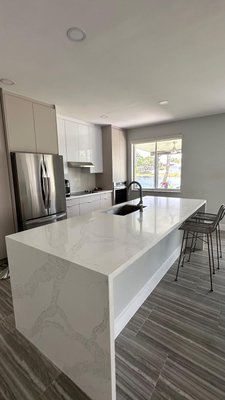 Modern Lakeview Kitchen Remodel - This kitchen transformation blends functionality and sophistication with a minimalist design. Warm taupe cabinetry, sleek white quartz countertops, and integrated modern appliances create a seamless, open space filled with natural light. Every detail — from the waterfall island to the soft neutral palette — was crafted to enhance daily living and elevate the heart of the home.