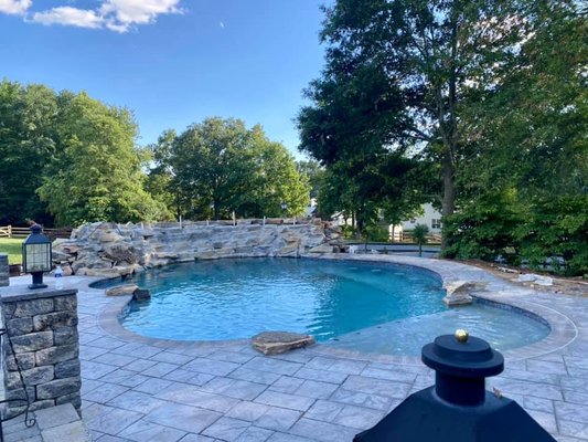 18 x 36 Custom Pool Installation - This rock waterfall pool is a stunning blend of natural beauty and functional design, transforming your backyard into a serene escape. The centerpiece is a handcrafted rock waterfall, where water cascades gracefully over textured stone, creating a soothing sound of flowing water. 18 x 36 Custom Pool Installation - This rock waterfall pool is a stunning blend of natural beauty and functional design, transforming your backyard into a serene escape. The centerpiece is a handcrafted rock waterfall, where water cascades gracefully over textured stone, creating a soothing sound of flowing water.