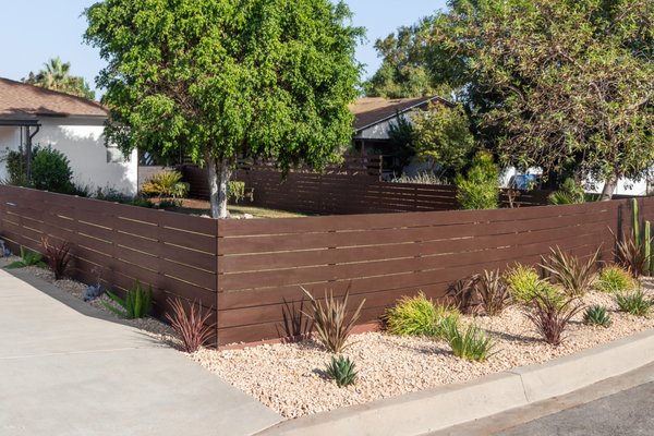 Desert Style Landscaping, before and after photos. - At this client's home we created a desert style landscape with 3/4" crushed gravel (and as always) weed fabric, horizontal Redwood fencing with a pressure-treated wood frame and a solid stain, Purple New Zealand Flax, Fountain Grasses, Blue Glow Agave, a San Pedro Cactus, and drip irrigation for water-saving purposes.
