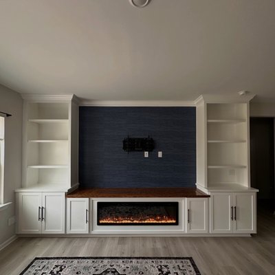 Custom Entertainment TV Wall - Elevate your living space with this stunning custom entertainment wall!

A beautifully designed built-in featuring elegant white cabinetry, open display shelving, rich wood countertops, and a dramatic textured navy accent wall. The sleek electric fireplace creates a warm, inviting focal point, while the clean architectural details and abundant storage bring together luxury, comfort, and functionality.

The contrast between the crisp white finishes, natural wood tones, and deep blue backdrop gives the room a sophisticated, modern feel with timeless character—the perfect centerpiece for relaxing, entertaining, and making memories