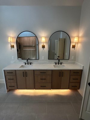 Master bath - Aura - This master bathroom underwent a complete transformation — from dated and confined to spacious, serene, and spa-like. The renovation included a full gut down to the studs, reimagining both layout and finishes for a sleek and modern design.
Key features of the remodel include:
Custom Double Vanity: A floating-style oak vanity with matte black hardware and under-cabinet LED accent lighting creates warmth and sophistication. Paired with integrated sinks, quartz countertops, and arched mirrors framed by elegant sconces.
Freestanding Soaking Tub: Positioned beneath the window with custom plantation shutters, the tub provides a beautiful focal point and a true place to unwind.
Luxury Walk-In Shower: Wrapped in vertical wood-look tile for texture and warmth, the shower features dual rain heads, a sleek matte black trim kit, and a minimalist linear drain.
Upgraded Lighting: Layered lighting includes modern pendant lights and warm-tone wall sconces to elevate the mood and ambiance.
Oversized Modern Tile Flooring: Neutral large-format floor tiles provide a clean, seamless look while offering durability and timeless elegance.
From layout to lighting, every detail was thoughtfully curated to blend high-end comfort with practical daily function — transforming this space into a peaceful retreat you’ll never want to leave. Master bath - Aura - This master bathroom underwent a complete transformation — from dated and confined to spacious, serene, and spa-like. The renovation included a full gut down to the studs, reimagining both layout and finishes for a sleek and modern design.
Key features of the remodel include:
Custom Double Vanity: A floating-style oak vanity with matte black hardware and under-cabinet LED accent lighting creates warmth and sophistication. Paired with integrated sinks, quartz countertops, and arched mirrors framed by elegant sconces.
Freestanding Soaking Tub: Positioned beneath the window with custom plantation shutters, the tub provides a beautiful focal point and a true place to unwind.
Luxury Walk-In Shower: Wrapped in vertical wood-look tile for texture and warmth, the shower features dual rain heads, a sleek matte black trim kit, and a minimalist linear drain.
Upgraded Lighting: Layered lighting includes modern pendant lights and warm-tone wall sconces to elevate the mood and ambiance.
Oversized Modern Tile Flooring: Neutral large-format floor tiles provide a clean, seamless look while offering durability and timeless elegance.
From layout to lighting, every detail was thoughtfully curated to blend high-end comfort with practical daily function — transforming this space into a peaceful retreat you’ll never want to leave.