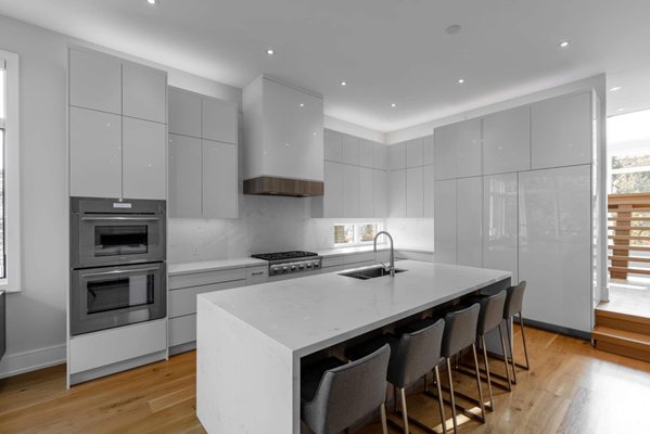 Kitchen Renovation in Mississauga by Kitchen Land - Kitchen Land was commissioned to transform a client’s home, with the primary focus on creating a spacious, open-concept kitchen. The client desired a large, functional kitchen with ample storage that seamlessly integrates with the surrounding architecture.
In response, we designed a sleek, contemporary two-tone kitchen, featuring white gloss slab cabinetry paired with a textured gray wood veneer island. The minimalist design conceals all appliances, including the refrigerator, using a handleless system with a modern push-to-open mechanism for a seamless finish.
The choice of white gloss was intentional, maximizing the effect of both natural and artificial light to brighten the space, while the upper cabinets reflect light throughout the home. We selected a quartz countertop that elegantly mimics marble, enhanced by a double waterfall island that serves as a focal point. To balance the cool tones, 7” wide plank engineered flooring in a natural finish was installed, adding warmth and sophistication to the overall design. Kitchen Renovation in Mississauga by Kitchen Land - Kitchen Land was commissioned to transform a client’s home, with the primary focus on creating a spacious, open-concept kitchen. The client desired a large, functional kitchen with ample storage that seamlessly integrates with the surrounding architecture.
In response, we designed a sleek, contemporary two-tone kitchen, featuring white gloss slab cabinetry paired with a textured gray wood veneer island. The minimalist design conceals all appliances, including the refrigerator, using a handleless system with a modern push-to-open mechanism for a seamless finish.
The choice of white gloss was intentional, maximizing the effect of both natural and artificial light to brighten the space, while the upper cabinets reflect light throughout the home. We selected a quartz countertop that elegantly mimics marble, enhanced by a double waterfall island that serves as a focal point. To balance the cool tones, 7” wide plank engineered flooring in a natural finish was installed, adding warmth and sophistication to the overall design.