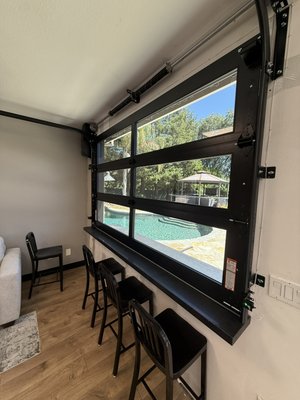 Custom door - This custom garage transformation features a built-in bar countertop paired with a full-view glass garage door, finished with powder-coated black track and hardware for a sleek, modern look. The perfect setup for entertaining, enjoying the view, and blending indoor comfort with outdoor living. Custom door - This custom garage transformation features a built-in bar countertop paired with a full-view glass garage door, finished with powder-coated black track and hardware for a sleek, modern look. The perfect setup for entertaining, enjoying the view, and blending indoor comfort with outdoor living.