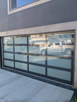 Custom color full view aluminum modern door - This beautiful house in Laguna Beach by the ocean has been remodeled in and out and the last piece was the garage door.
The existing door was made of steel and was noisy, the opener was an old overhead door.
We tried to match the new door to the modern look of the house so we chose full view glass and aluminum door.
The trim color was grey and because the manufacturer doesn't offer it as a stock color we powder coat the frame to match the trim.
Inside, to save space and create a clean look we installed a smart side mount opener and we removed all the brackets and rail from the ceiling. Custom color full view aluminum modern door - This beautiful house in Laguna Beach by the ocean has been remodeled in and out and the last piece was the garage door.
The existing door was made of steel and was noisy, the opener was an old overhead door.
We tried to match the new door to the modern look of the house so we chose full view glass and aluminum door.
The trim color was grey and because the manufacturer doesn't offer it as a stock color we powder coat the frame to match the trim.
Inside, to save space and create a clean look we installed a smart side mount opener and we removed all the brackets and rail from the ceiling.