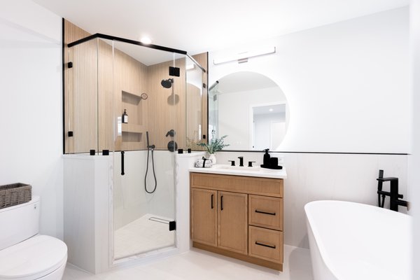 Jefferson Park Complete Modern Bathroom Remodel - This complete bathroom renovation in Chicago by 4Ever Remodeling features a full-scale spa transformation. The project includes a custom corner glass shower with MSI Urban Slats Natural fluted accent walls, Roca Lasa White unpolished main floor tile, a modern freestanding soaking tub, and a Forevermark Petit Oak vanity topped with New Stone Da Vinci Gray quartz. Finished with Gibson matte black hardware and a backlit circular mirror, this layout represents a complete primary bathroom overhaul.