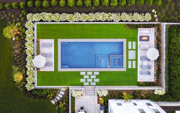 Low-Maintenance Montclair Oasis - Montclair, NJ - In Montclair, NJ, we transformed a challenging, sloped backyard into an exquisite pool and patio
area that has become the homeowner’s dream retreat. Initially faced with obstacles such as
mature trees, steep slopes, and various site challenges, our team designed and executed a
stunning solution. The centerpiece of this transformation is a sleek, Hamptons-style pool,
surrounded by synthetic turf.
Our crew installed a new patio along the back of the home, creating a versatile outdoor living
area separate from the pool. This strategically placed patio offers a seamless transition to the
pool area, enhancing accessibility and flow. To cater to diverse needs, we included two distinct
zones around the pool: one designed for sunbathing and another for relaxed conversations by
the fire.
To complete the vision of a private oasis, we needed to build large retaining walls to create a
level area for the pool. We enhanced the area with a diverse selection of plants, shrubs, and
trees. The multi-tiered garden features an array of hydrangeas, junipers, boxwoods, arborvitae,
schip laurels, and ornamental grasses, evoking the charm of a well-tended sanctuary. This rich
variety not only adds visual interest but also provides maximum privacy, allowing the family to
enjoy their outdoor space with complete seclusion. Low-Maintenance Montclair Oasis - Montclair, NJ - In Montclair, NJ, we transformed a challenging, sloped backyard into an exquisite pool and patio
area that has become the homeowner’s dream retreat. Initially faced with obstacles such as
mature trees, steep slopes, and various site challenges, our team designed and executed a
stunning solution. The centerpiece of this transformation is a sleek, Hamptons-style pool,
surrounded by synthetic turf.
Our crew installed a new patio along the back of the home, creating a versatile outdoor living
area separate from the pool. This strategically placed patio offers a seamless transition to the
pool area, enhancing accessibility and flow. To cater to diverse needs, we included two distinct
zones around the pool: one designed for sunbathing and another for relaxed conversations by
the fire.
To complete the vision of a private oasis, we needed to build large retaining walls to create a
level area for the pool. We enhanced the area with a diverse selection of plants, shrubs, and
trees. The multi-tiered garden features an array of hydrangeas, junipers, boxwoods, arborvitae,
schip laurels, and ornamental grasses, evoking the charm of a well-tended sanctuary. This rich
variety not only adds visual interest but also provides maximum privacy, allowing the family to
enjoy their outdoor space with complete seclusion.