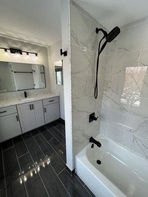 Modern Luxury Transformation - A complete bathroom remodel featuring large-format white marble tiles with delicate grey veining along the walls and bathtub surround. Complete with dark-tiled flooring for contrast, an integrated bath recess, and refined LED vanity lighting that illuminates the crisp, modern aesthetic. Modern Luxury Transformation - A complete bathroom remodel featuring large-format white marble tiles with delicate grey veining along the walls and bathtub surround. Complete with dark-tiled flooring for contrast, an integrated bath recess, and refined LED vanity lighting that illuminates the crisp, modern aesthetic.