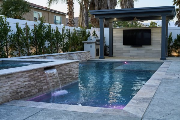 Eastvale Exquisite Linear - This sleek liner pool combines simplicity with custom luxury. It features a fully automated chemical management system for effortless maintenance, along with a custom outdoor shower for added convenience. A freestanding patio cover includes a tailored TV wall designed to match the pool’s finishes, creating a seamless look. A modern outdoor fireplace completes the space, perfect for relaxing or entertaining in style.