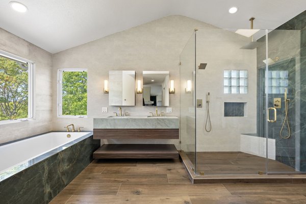 From Traditional to Contemporary Bathroom Remodel by PBH Builders in Encinitas, CA - We recently completed this full primary bathroom remodel in Encinitas, CA, where we at PBH Builders transformed a traditional bathroom into a refined contemporary retreat tailored to our client's vision. While the original space offered a generous layout and plenty of natural light, its dark stone finishes, oversized cabinetry, and traditional fixtures made the room feel dated. Our objective was to preserve the spacious layout while introducing premium materials, cleaner lines, and a more inviting design that better complemented the home.
The remodel began with a complete demolition, allowing us to reconfigure the space with a modern, cohesive design. We installed large-format porcelain wall tile in soft neutral tones to brighten the room, while wood-look porcelain flooring introduced warmth and natural texture. A custom floating walnut vanity became the centerpiece of the bathroom, paired with a quartzite countertop that showcases subtle veining and timeless character. Brushed brass faucets, hardware, and sconces were selected to add warmth and contrast, creating a sophisticated finish that ties the entire space together.
The shower was redesigned as a luxurious walk-in enclosure with frameless glass that keeps the room feeling open and spacious. Dramatic quartzite slab walls create a striking focal point, complemented by textured porcelain tile for added depth and visual interest. We incorporated a built-in bench, recessed storage niche, dual rainfall showerheads, and matching handheld fixtures to maximize both comfort and functionality. The soaking tub was also refreshed with a coordinating quartzite surround, allowing every element of the bathroom to flow seamlessly while taking full advantage of the natural light from the surrounding windows.
The completed space now feels brighter, more open, and thoughtfully designed from every angle. The combination of natural stone, warm wood tones, soft porcelain tile, and brushed brass finishes creates a balanced contemporary aesthetic that is both elegant and practical. Every feature was selected with purpose, resulting in a bathroom that delivers comfort, functionality, and lasting value.
If you're considering a custom bathroom remodel, connect with PBH Builders to explore premium materials, personalized design solutions, and expert craftsmanship that transforms your vision into a space built specifically for your home. From Traditional to Contemporary Bathroom Remodel by PBH Builders in Encinitas, CA - We recently completed this full primary bathroom remodel in Encinitas, CA, where we at PBH Builders transformed a traditional bathroom into a refined contemporary retreat tailored to our client's vision. While the original space offered a generous layout and plenty of natural light, its dark stone finishes, oversized cabinetry, and traditional fixtures made the room feel dated. Our objective was to preserve the spacious layout while introducing premium materials, cleaner lines, and a more inviting design that better complemented the home.
The remodel began with a complete demolition, allowing us to reconfigure the space with a modern, cohesive design. We installed large-format porcelain wall tile in soft neutral tones to brighten the room, while wood-look porcelain flooring introduced warmth and natural texture. A custom floating walnut vanity became the centerpiece of the bathroom, paired with a quartzite countertop that showcases subtle veining and timeless character. Brushed brass faucets, hardware, and sconces were selected to add warmth and contrast, creating a sophisticated finish that ties the entire space together.
The shower was redesigned as a luxurious walk-in enclosure with frameless glass that keeps the room feeling open and spacious. Dramatic quartzite slab walls create a striking focal point, complemented by textured porcelain tile for added depth and visual interest. We incorporated a built-in bench, recessed storage niche, dual rainfall showerheads, and matching handheld fixtures to maximize both comfort and functionality. The soaking tub was also refreshed with a coordinating quartzite surround, allowing every element of the bathroom to flow seamlessly while taking full advantage of the natural light from the surrounding windows.
The completed space now feels brighter, more open, and thoughtfully designed from every angle. The combination of natural stone, warm wood tones, soft porcelain tile, and brushed brass finishes creates a balanced contemporary aesthetic that is both elegant and practical. Every feature was selected with purpose, resulting in a bathroom that delivers comfort, functionality, and lasting value.
If you're considering a custom bathroom remodel, connect with PBH Builders to explore premium materials, personalized design solutions, and expert craftsmanship that transforms your vision into a space built specifically for your home.