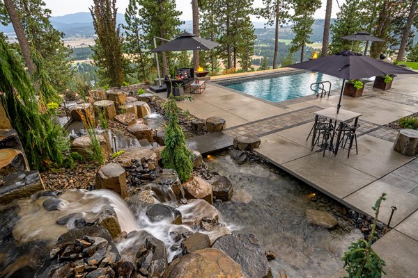 Spokane Landscape Architect Project - This mountain home retreat is one of Alderwood's largest projects in the Spokane area. With a large water feature, pool, and stunning views, it is no wonder this has become one of our favorites!

When these clients contacted Alderwood, they expressed a desire for a design that took advantage of their large property and 360-degree views without taking away from the grandeur of their craftsman-style home.

From an architectural standpoint, the main challenge of this property was to connect the front yard landscaping (which included two basalt water features and a paver driveway) to the central landscaping around the side and back of the property. Our design team solved this issue by implementing a massive basalt boulder retaining wall with custom stone steps that worked into an extensive water feature system. The pavers around the property complemented the home's style and provided a natural flow from the interior outside.

For added interest, elements of fire were placed around the edge of the landscape. Fire cauldrons and a sunken fire pit provided entertainment features while still preserving the distant lake view.

Overall, our clients said they could not be more pleased with the results and constantly invite friends to their new paradise.

Design Elements Included
Expansive Water Feature Retaining Wall

Custom Pond With Negative Edge

Sunken Fire Pit and Patio

Hand-Picked Basalt Stone Steps

Custom Paver Driveway

LED Night Lighting

Custom Lit Pool

Fire Cauldrons