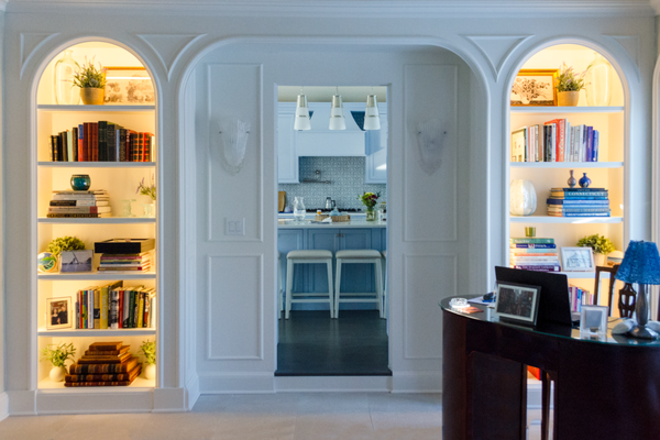Built-Ins Framing a Dreamy Kitchen - These custom-built shelves add warmth and sophistication with their illuminated displays of books, art, and greenery. Framing the entrance to a bright blue kitchen, the built-ins seamlessly blend function and style, creating a welcoming and curated look. A perfect design element to elevate any transitional space in your home!