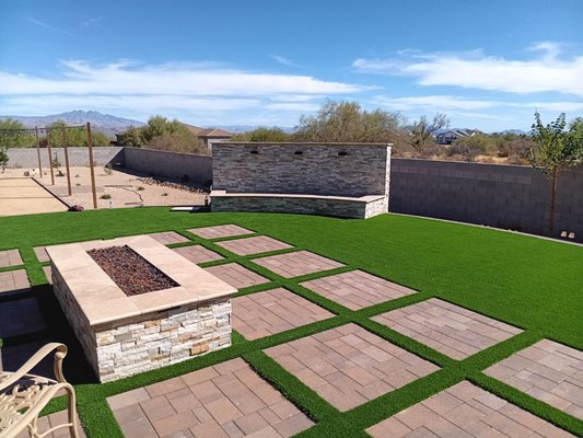 Backyard Transformation in Rio Verde - We installed a custom drip irrigation system to support lush new plantings, then elevated the entertainment game with a BBQ island wrapped in travertine and an extended bar for effortless hosting. A fire pit with a bullnose travertine cap and custom firebar sets the vibe, while a statement water feature wall with copper scuppers and tiled basin adds soothing ambiance.

And we didn’t stop there:
- Modern step pads for function & flair
- Fresh planting and LED lighting to create ambiance
- Rich synthetic turf for year-round greenery with no hassle