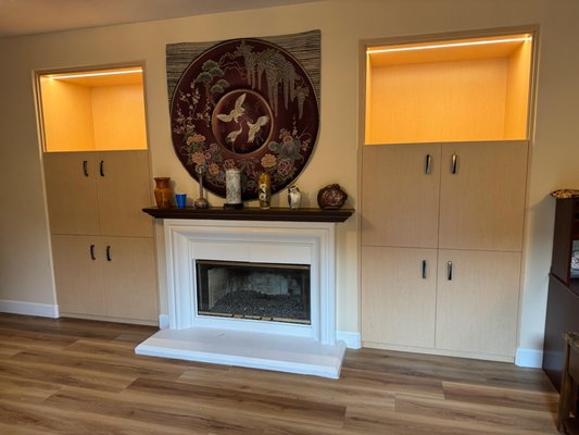 Maple Built-In Cabinets with LED Lights - These built-in niches were fully transformed into elegant, functional custom cabinetry that blends seamlessly with the home’s interior. What used to be open recesses with simple shelves is now a warm, cohesive storage solution that elevates the entire space.
The cabinets were designed specifically to fit into the existing niches with a clean, built-in look, providing a cozy atmosphere and excellent storage capability. The finish was chosen in a soft maple tone to match the home’s flooring and decor, creating a unified visual flow. Warm LED lighting was added inside the upper open sections near the fireplace to highlight the beautiful display areas and bring depth and ambiance to the room.
The two illuminated open spaces above the cabinets were purposefully created to showcase large decorative vases and art pieces, turning them into focal points rather than just storage. The result is a refined, functional upgrade that enhances both the practicality and the aesthetic harmony of the home. Maple Built-In Cabinets with LED Lights - These built-in niches were fully transformed into elegant, functional custom cabinetry that blends seamlessly with the home’s interior. What used to be open recesses with simple shelves is now a warm, cohesive storage solution that elevates the entire space.
The cabinets were designed specifically to fit into the existing niches with a clean, built-in look, providing a cozy atmosphere and excellent storage capability. The finish was chosen in a soft maple tone to match the home’s flooring and decor, creating a unified visual flow. Warm LED lighting was added inside the upper open sections near the fireplace to highlight the beautiful display areas and bring depth and ambiance to the room.
The two illuminated open spaces above the cabinets were purposefully created to showcase large decorative vases and art pieces, turning them into focal points rather than just storage. The result is a refined, functional upgrade that enhances both the practicality and the aesthetic harmony of the home.