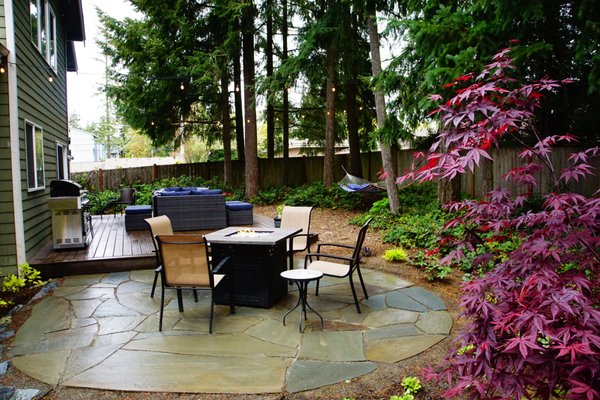 Woodland Entertaining Space in Shoreline - Our clients had a back and side yard of patchy lawn with a concrete slab off the back door (see the “Before” photos at bottom!).

They wanted a space to relax in the hammock, to enjoy a firepit on a chilly evening, or to host a 6-8 person dinner party on the back deck.

We designed:
-A low-maintenance Trex deck
-Flagstone firepit area
-New low-maintenance, shade-loving plantings
-Woodchip path through the new side garden
-Microspray irrigation to ensure the new garden thrived

And then our clients hung their favorite hammock from a couple of tall douglas firs. Voila!