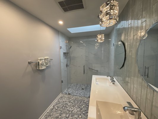 Bathroom remodeling in Western Springs, IL - Bathroom Remodeling in Western Springs – Complete Transformation

Sunny Construction & Remodeling recently completed a full bathroom renovation for a homeowner in Western Springs, IL. The original space had an outdated corner shower, oversized jacuzzi tub, gold trim, older cabinets, and marble-pattern flooring. Our team redesigned the bathroom to create a modern, open, and functional spa-like layout.

We removed the old tub platform and enclosed shower to open the space and improve flow. A new curbless walk-in shower was constructed with large marble-look wall tile, a custom quartz shower bench, a recessed niche with mosaic accents, and upgraded plumbing fixtures for better comfort and accessibility. The new shower design gives the room a clean, elegant look while providing safe and easy entry.

The vanity area was upgraded with a sleek double-sink countertop, new faucets, and modern cabinetry in a soft gray finish. We added a tall storage cabinet to maximize organization without taking up floor space. A textured vertical accent tile behind the mirrors brings dimension and visual interest, while new LED recessed lighting and crystal pendant fixtures brighten the room and highlight the updated finishes.

The old flooring was replaced with durable hexagon mosaic tile, tying the entire design together with a fresh, contemporary style. Fresh paint, updated trim, and careful attention to detail completed the transformation.

This Western Springs bathroom remodel blends modern design with practical features, creating a beautiful and functional space the homeowners will enjoy for years. Sunny Construction & Remodeling is proud to deliver high-quality craftsmanship for every project in Western Springs and the surrounding Chicago suburbs.