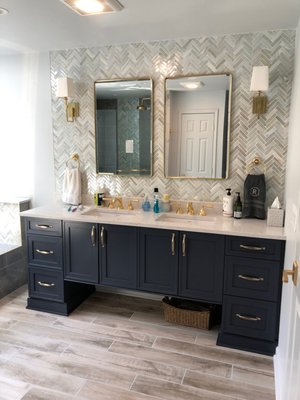 Primary Bathroom Remodel - This New Jersey master bath was fairly large but had an awkward configuration. Working within the same footprint, we changed the layout to increase the size of the tub and shower, while reducing the linen closet. Layout and design were a collaborative effort with the homeowner and a Monk's designer based in our Fanwood-Scotch Plains showroom.
A large window was added above the new jetted tub bringing in loads of natural light and a pretty view of the backyard. Wood-look porcelain tile was installed in the floor. On the walls and in the shower, large format gray and white tiles were installed. Chevron accent tile is found vertically in the shower, behind the toilet, as part of the tub surround and as a full wall behind the vanity. Italian brass hardware and fixtures were used throughout. A gorgeous navy vanity with quartz top ads a pop of color to the neutral room. The same quartz was installed around the tub and on the half wall between the tub and shower.
The result is a stunning new master bathroom! Primary Bathroom Remodel - This New Jersey master bath was fairly large but had an awkward configuration. Working within the same footprint, we changed the layout to increase the size of the tub and shower, while reducing the linen closet. Layout and design were a collaborative effort with the homeowner and a Monk's designer based in our Fanwood-Scotch Plains showroom.
A large window was added above the new jetted tub bringing in loads of natural light and a pretty view of the backyard. Wood-look porcelain tile was installed in the floor. On the walls and in the shower, large format gray and white tiles were installed. Chevron accent tile is found vertically in the shower, behind the toilet, as part of the tub surround and as a full wall behind the vanity. Italian brass hardware and fixtures were used throughout. A gorgeous navy vanity with quartz top ads a pop of color to the neutral room. The same quartz was installed around the tub and on the half wall between the tub and shower.
The result is a stunning new master bathroom!